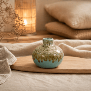 Turquoise knopvaasje met bruine dripglazuur op een houten plank in een warme, sfeervolle setting.