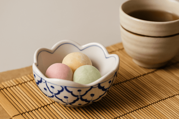 Klein Thais kommetje in bloemvorm met mochi dessert en een kopje thee op een bamboemat.