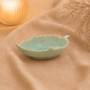 Blauw keramisch bladschaaltje van 17 cm met bladreliëf in warme sfeersetting op beige stof.