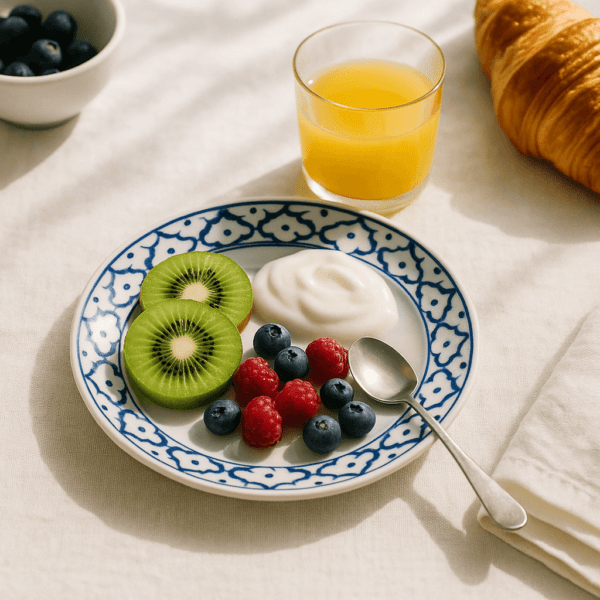 Blauw-wit bord van 16 cm met kiwi, blauwe bessen, frambozen en yoghurt, naast een croissant