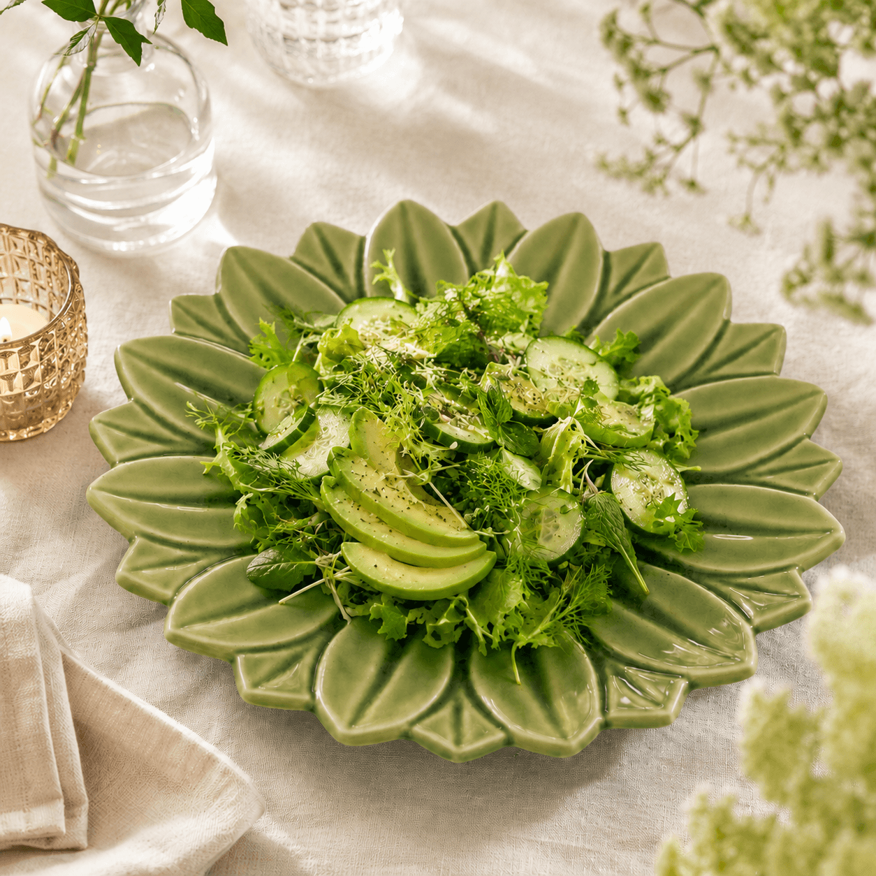 Groen keramisch lotus bord van 27 cm met groene salade op een licht gedekte tafel.