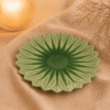 Groen keramisch lotus bord van 27 cm op beige stof in een warme sfeersetting met zachte verlichting.