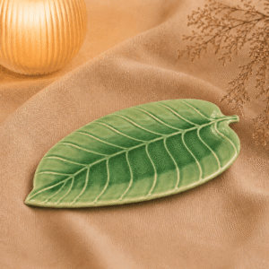 Groene keramische schaal in bladvorm van 24 cm op beige stof in een warme sfeersetting.