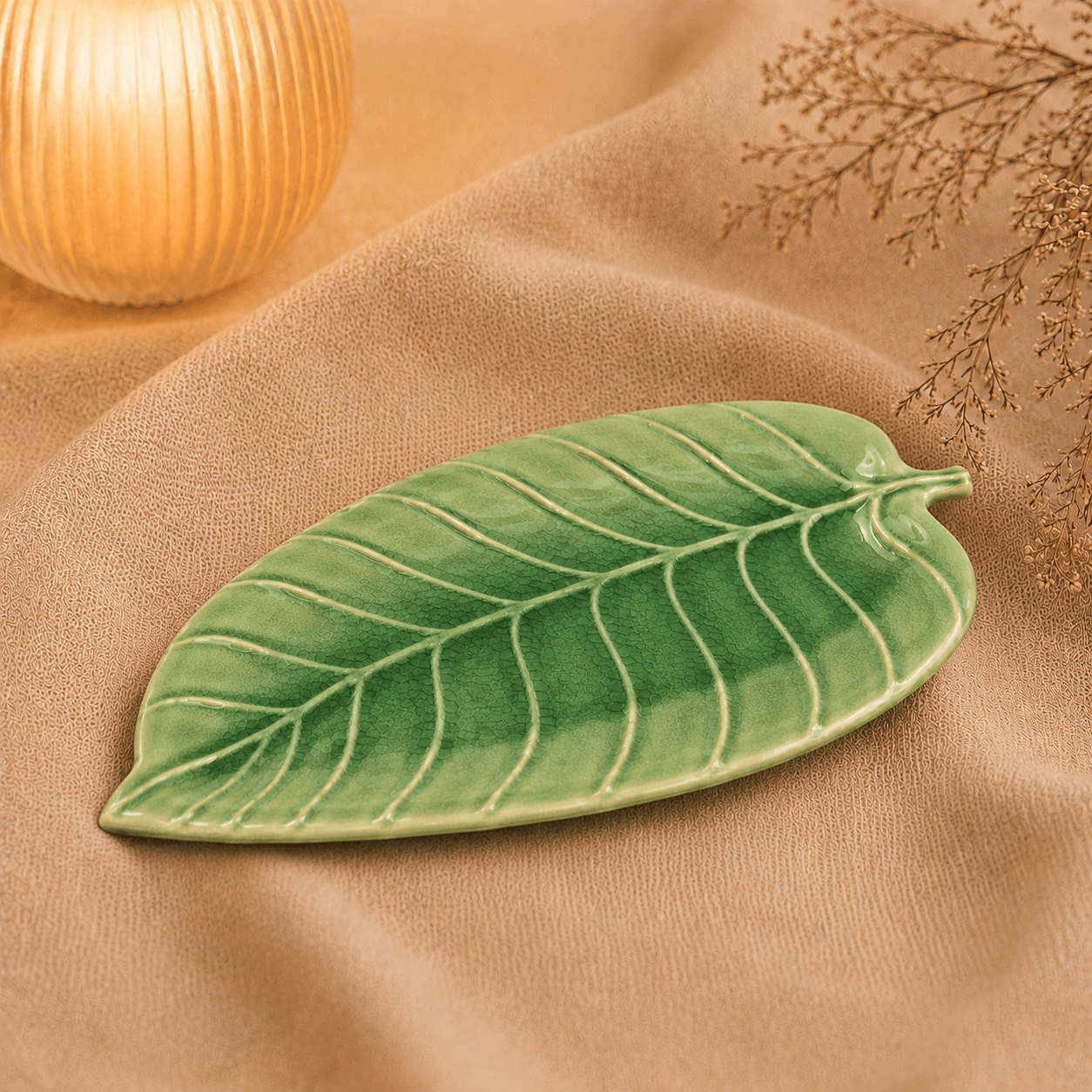 Groene keramische schaal in bladvorm van 24 cm op beige stof in een warme sfeersetting.