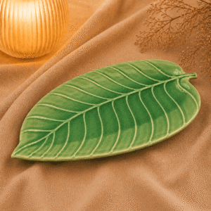 Groene keramische schaal in bladvorm van 28 cm op beige stof in een warme sfeersetting met zachte verlichting.
