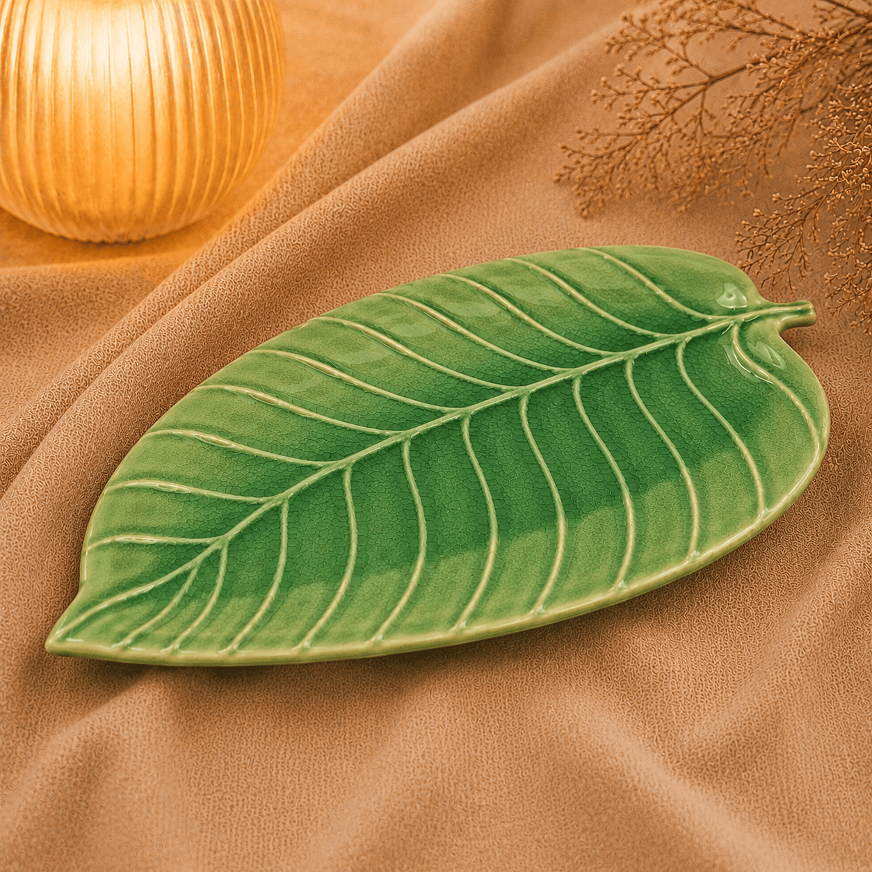 Groene keramische schaal in bladvorm van 28 cm op beige stof in een warme sfeersetting met zachte verlichting.