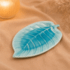 Blauwe keramische schaal in bladvorm van 21 cm op beige stof in een warme sfeersetting.