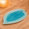 Blauwe keramische schaal in bladvorm van 26 cm op beige stof met warme verlichting en droogbloemen.