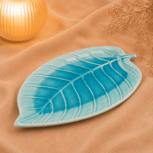 Blauwe keramische schaal in bladvorm van 26 cm op beige stof met warme verlichting en droogbloemen.