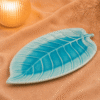 Blauwe keramische schaal in bladvorm van 28 cm op beige stof in een warme sfeersetting.