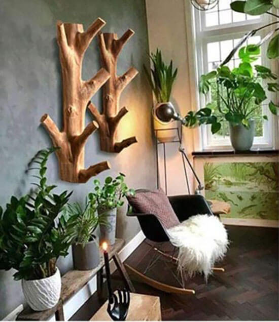 Twee houten takkenhouten wandkapstokken aan de muur in een groene plantenhoek, met stoel, lamp en raam op de achtergrond.