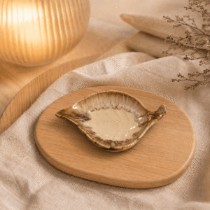Crème bruin keramisch schaaltje in bladvorm op houten plateau in warme sfeersetting met lamp en beige stof.