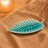 Blauwe keramische bladschaal van 27.5 cm op beige stof in een warme sfeersetting met decoratieve takjes.