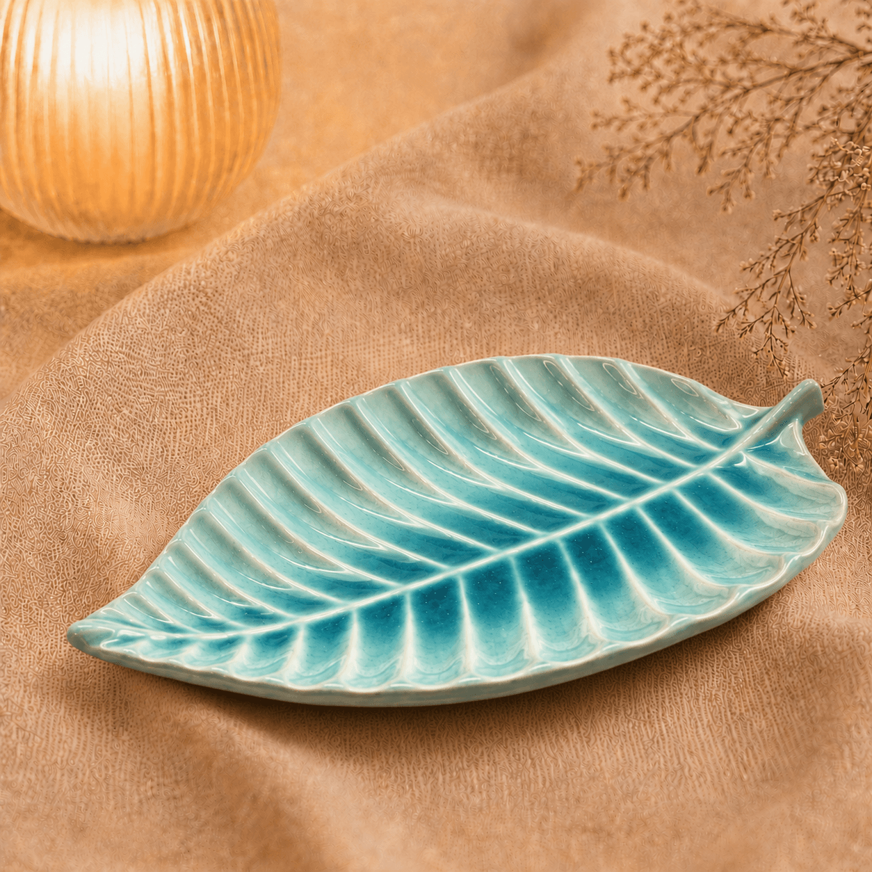 Blauwe keramische bladschaal van 28 cm op beige stof in een warme sfeersetting met decoratieve takjes.