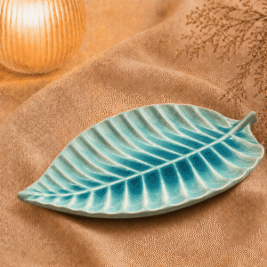 Blauwe keramische bladschaal van 31 cm op beige stof in een warme sfeersetting met zachte verlichting.