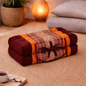 Opgevouwen Thais meditatiekussen in bordeaux en oranje met licht traditioneel patroon in een warme en rustgevende interieursetting.