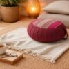 Rond Thais meditatiekussen in bordeaux en roze met traditioneel patroon in een warme, rustgevende ruimte.