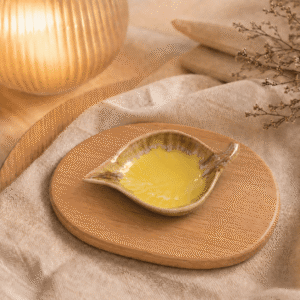 Geel keramisch schaaltje in bladvorm op houten plateau in warme sfeersetting met beige stof en sfeerlamp.