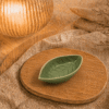 Groen keramisch schaaltje in bladvorm op houten plateau in warme sfeersetting met lamp en decoratieve takjes.