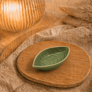 Groen keramisch schaaltje in bladvorm op houten plateau in warme sfeersetting met lamp en decoratieve takjes.