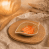Oranje keramisch schaaltje in bladvorm op houten plateau in warme sfeersetting met beige stof en sfeerlamp.