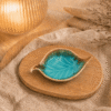 Turquoise crèmekleurig keramisch schaaltje in bladvorm op houten plateau in warme sfeersetting met lamp en beige stof.