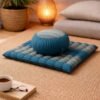 Blauw grijze zabutan mat met zafu meditatiekussen in warme woonkamer setting op kleed.