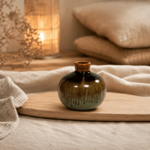 Rond keramieken knopvaasje met donkerbruin en mintgroen dripglazuur op een houten plank in een warme, natuurlijke sfeersetting.