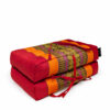 Draagbaar meditatiekussen rood oranje met etnisch patroon, opgevouwen met draaglinten zichtbaar.