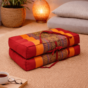 Opgevouwen Thais meditatiekussen in rood en oranje met goudkleurig traditioneel patroon in een warme en rustgevende interieursetting.