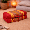 Opgevouwen Thais meditatiekussen in rood en oranje met goudkleurig traditioneel patroon in een warme en rustgevende interieursetting.