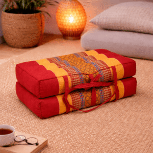 Opgevouwen Thais meditatiekussen in rood en oranje met goudkleurig traditioneel patroon in een warme en rustgevende interieursetting.