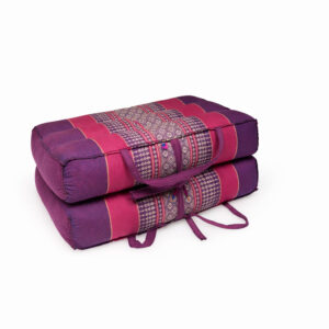Opgevouwen paars-roze meditatiekussen met traditioneel patroon en draaglint, vrijstaand op witte achtergrond.