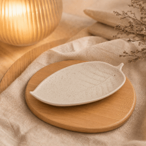 Bladschaal van naturel keramiek op een houten onderzetter met warme verlichting, beige textiel en natuurlijke decoratie.