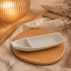 Bootvorm schaal gespikkeld wit met twee vakken op een houten onderzetter met warme verlichting en beige textiel.