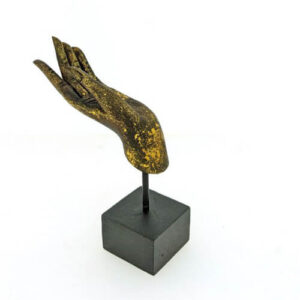 Zwart-gouden hand van Boeddha in abhaya mudra op zwarte voet tegen lichte achtergrond.