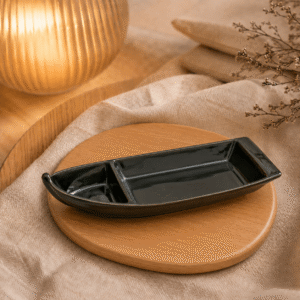 Bootvorm schaal zwart met twee vakken op een houten onderzetter met warme verlichting, beige textiel en natuurlijke decoratie.