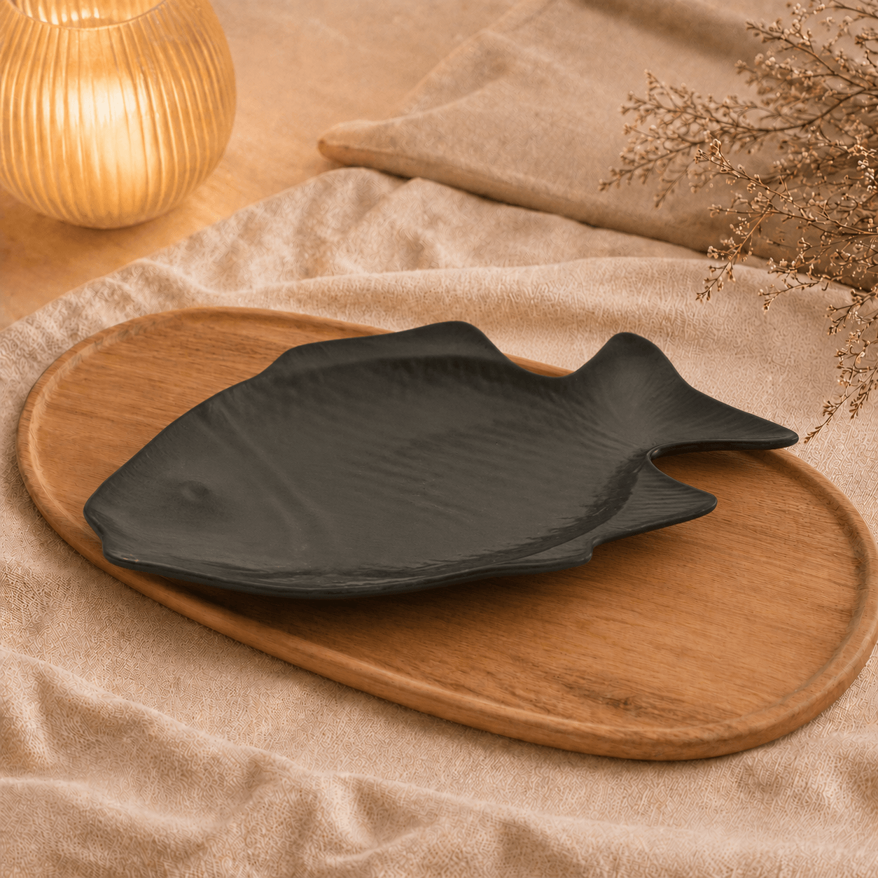 Zwart keramisch visbord van 38 cm op een houten dienblad met beige stof en warme sfeerverlichting.