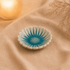 Blauw keramisch zonnebloem schaaltje op beige stof in een warme sfeersetting met zachte verlichting.