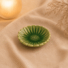 Groen keramisch zonnebloem schaaltje op beige stof in een warme sfeersetting met sfeervolle verlichting.