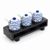 Blauw-witte Thaise kruidenset met drie keramische potjes, deksels en lepeltjes in een zwarte houten houder.