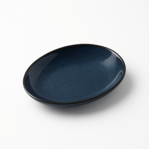 Diep donkerblauwe keramische ovale schaal met subtiel korrelig glazuur, gefotografeerd op een witte achtergrond