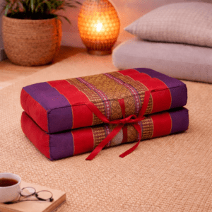 Opgevouwen Thais meditatiekussen in rood en paars met traditioneel patroon in een warme en rustgevende interieursetting.