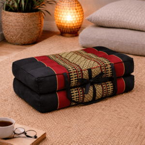 Opgevouwen Thais meditatiekussen in zwart en rood met goudkleurig traditioneel patroon in een warme en rustgevende interieursetting.