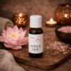 Flesje lotus massageolie op houten plank met roze lotusbloem en badzout in warme wellnesssetting.