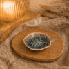 Blauw-grijs keramisch bladschaaltje op een houten dienblad in een warme sfeersetting met zachte verlichting.