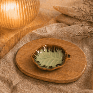 Groen-bruin keramisch bladschaaltje op een houten dienblad in een warme sfeersetting met zachte verlichting.