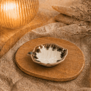 Wit-crème keramisch bladschaaltje op een houten dienblad in een warme sfeersetting met zachte verlichting.
