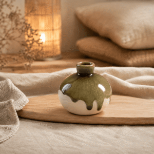 Klein rond keramieken knopvaasje in crème en olijfgroen met dripglazuur op een houten plank in een warme, natuurlijke sfeersetting.