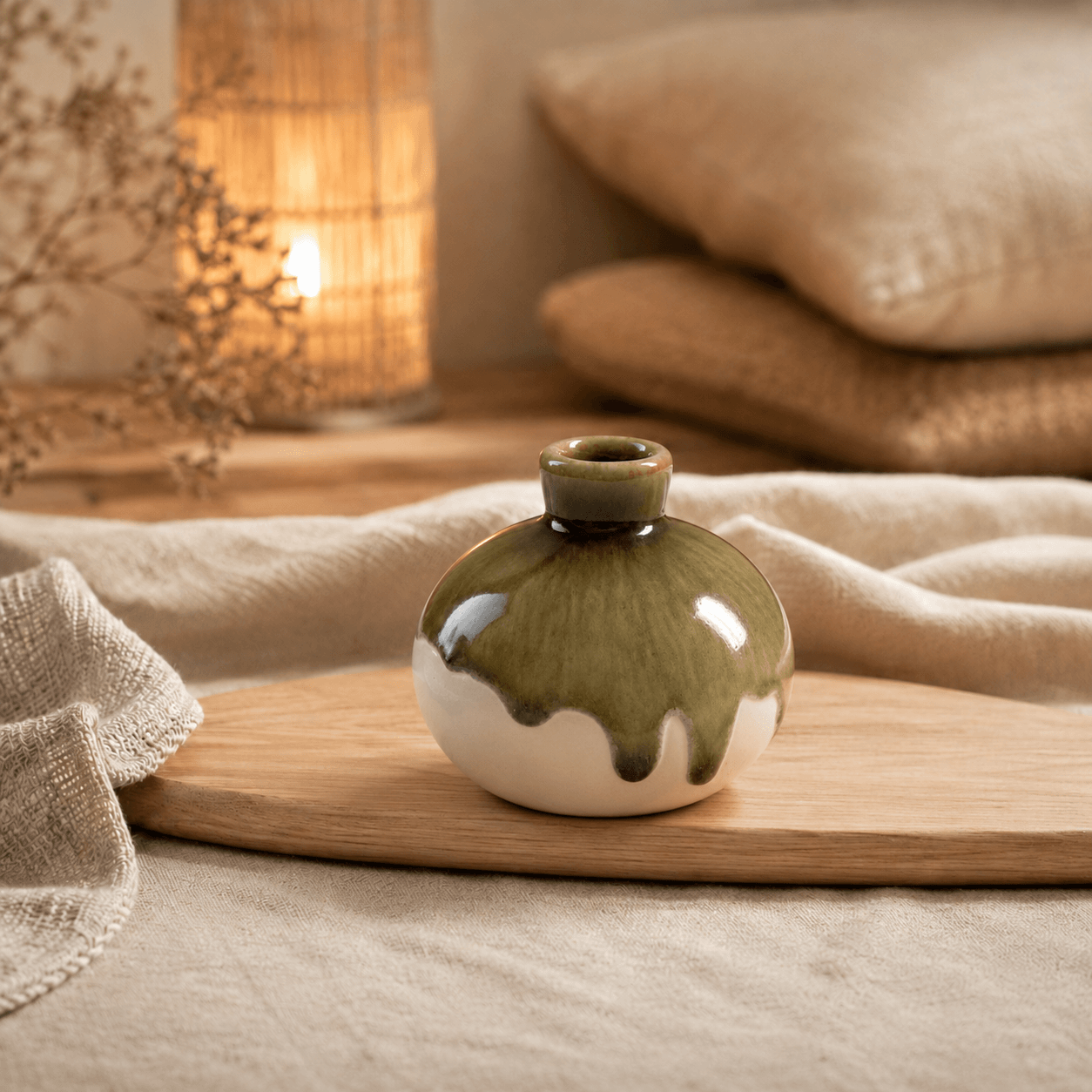 Klein rond keramieken knopvaasje in crème en olijfgroen met dripglazuur op een houten plank in een warme, natuurlijke sfeersetting.